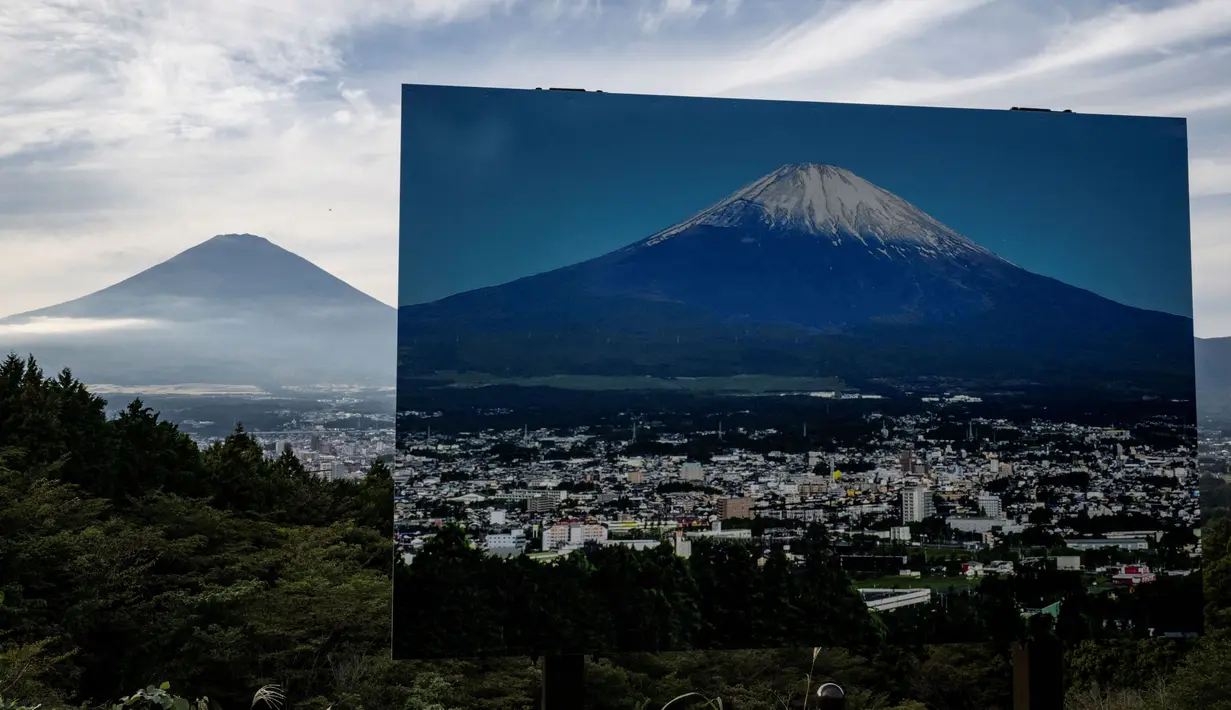 Sebuah penanda dengan foto Gunung Fuji dengan puncak yang tertutup salju terlihat di sebuah titik pandang berlatar belakang puncak Gunung Fuji yang tidak tertutup salju di Gotemba, prefektur Shizuoka, Jepang pada tanggal 31 Oktober 2024. (Yuichi YAMAZAKI/AFP)