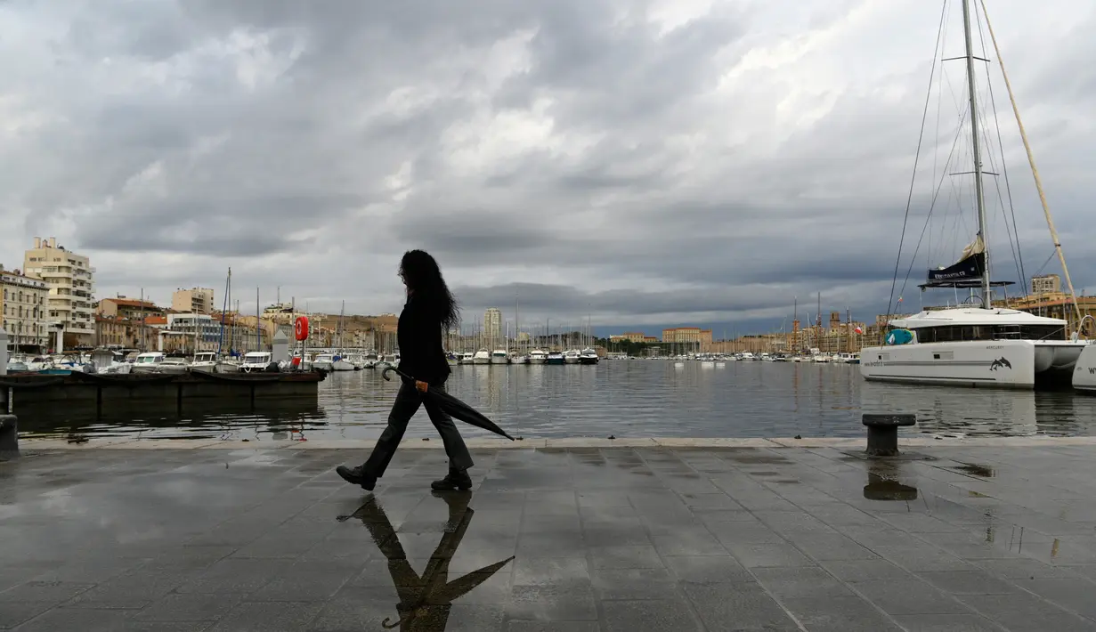 Seorang wanita berjalan dengan payungnya di Vieux-Port di Marseille, Prancis selatan,  Senin (4/10/2021). Wilayah Prancis selatan dalam siaga untuk hujan lebat dan banjir. (AFP Photo/Nicolas Tucat)