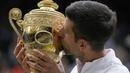 Petenis Serbia, Novak Djokovic cium Piala Wimbledon usai kalahkan petenis Italia, Matteo Berrettini di partai puncak tunggal putra. Kemenangan ini mengantarkan Djokovic menyamai rekor Nadal dan Federer sebagai petenis yang mampu mendapatkan 20 gelar Grand Slam. (Foto: AP/Kirsty Wigglesworth)