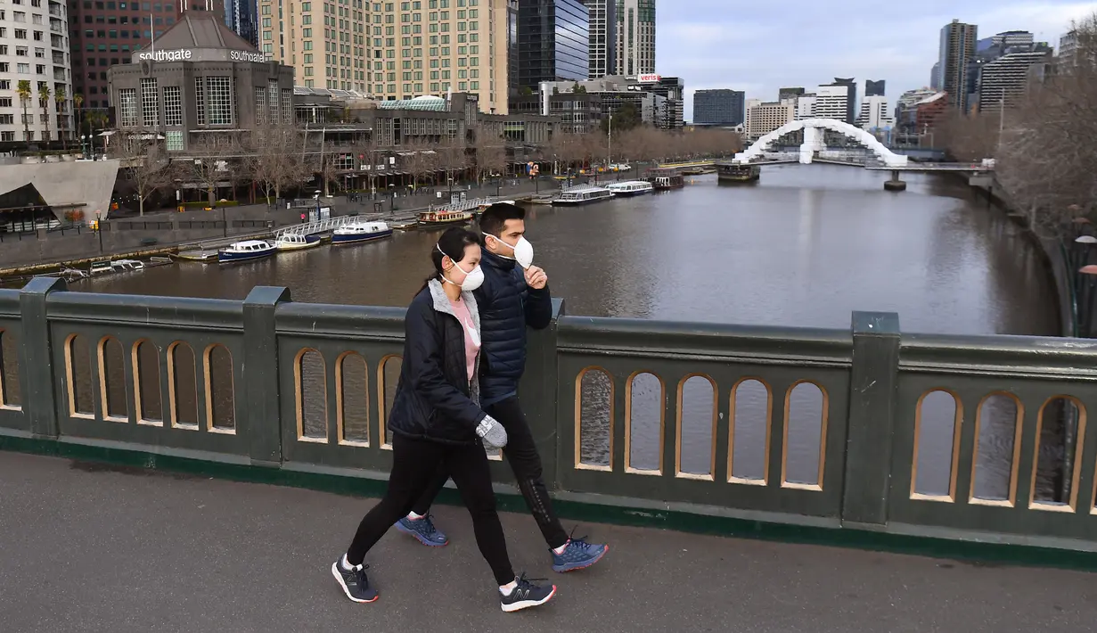 Orang-orang dengan masker berjalan di jembatan yang melintasi Sungai Yarra pada hari pertama wajib masker, di Melbourne Kamis (23/7/2020). Penduduk kota terpadat kedua di Australia, Melbourne, diwajibkan mengenakan masker saat meninggalkan rumah untuk mencegah penyebaran COVID-19. (William WEST/AFP)
