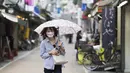 Seorang wanita dengan masker wajah berjalan melalui jalan perbelanjaan di tengah hujan di Tokyo (15/10/2020). Ibukota Jepang mengonfirmasi lebih dari 280 kasus virus korona baru pada hari Kamis. (AP Photo/Hiro Komae)