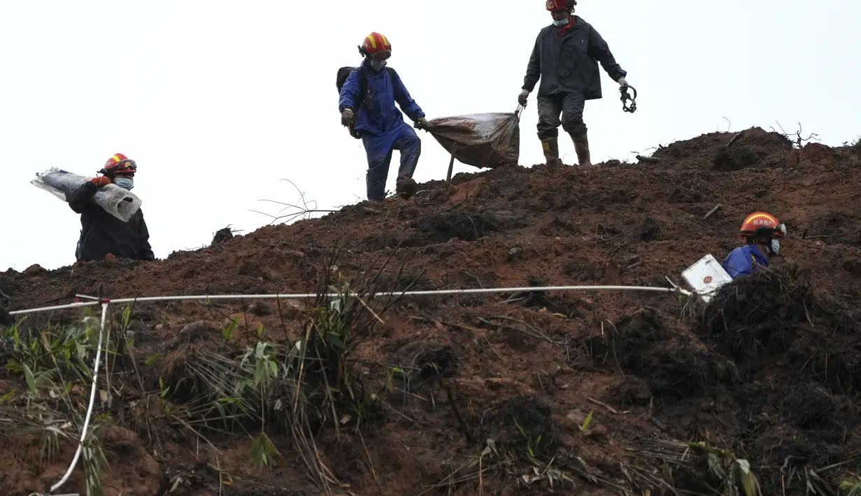 Pekerja darurat yang membawa barang-barang yang dibungkus tas turun dari lereng bukit setelah melakukan operasi pencarian di dekat lokasi kecelakaan pesawat Boeing 737-800 milik China Eastern Airlines di desa Molang, di provinsi Guangxi, China barat daya, Rabu (24/3/2022). (AP Photo/Ng Han Guan)