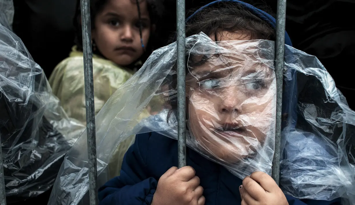 Seorang anak pengungsi tertutup jas hujan menunggu antrean mendapatkan kamp di Presevo, (7/10/2015). Foto ini pemenang '1st prize singles' World Press Photo Awards 2016 kategori People karya Matic Zorman berjudul 'Waiting to Register'. (Reuters via WPP)