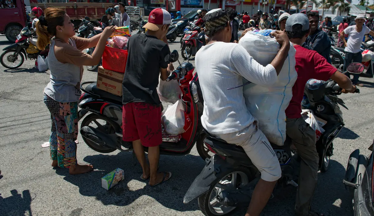 Warga membawa kebutuhan pokok menggunakan motor setelah menjarah toko swalayan menyusul gempa dan tsunami di Palu, Sulawesi Tengah, Minggu (30/9). Warga terpaksa mengambil karena mereka juga membutuhkan makanan dan air bersih. (AFP PHOTO/BAY ISMOYO)