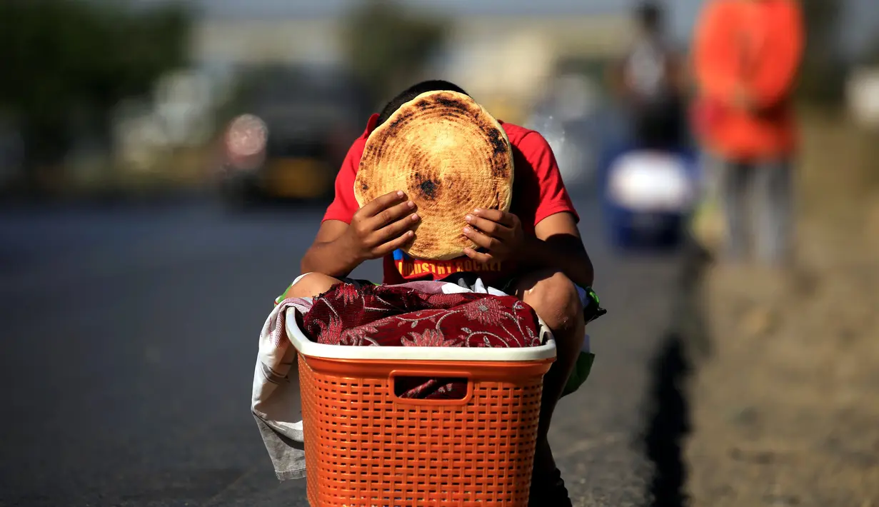 Issaac (8), memegang sepotong roti tradisional yang dijajakannya di tepi jalan raya di pinggiran Algiers, Aljazair, 13 Juni 2016. Selama bulan Ramadan, sejumlah anak membantu orangtuanya menjajakan roti di kawasan ini. (REUTERS/Zohra Bensemra)