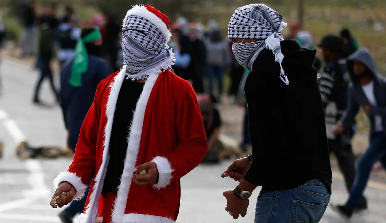 Seorang demonstran Palestina mengenakan kostum Santa Claus bersiap melempar batu ke arah pasukan keamanan Israel saat terjadi bentrokan di pos pemeriksaan Atarot di pinggiran utara Yerusalem (19/12). (AFP Photo/Abbas Momani)