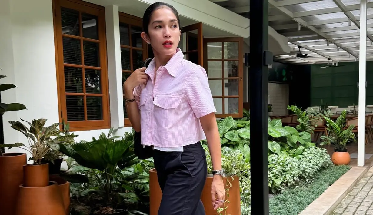 Ussy tampil mengenakan atasan cropped berkerah bernuansa merah muda, celana panjang hitam, alas kaki putih, dan tas hitam. [Foto: Instagram/ussypratama]