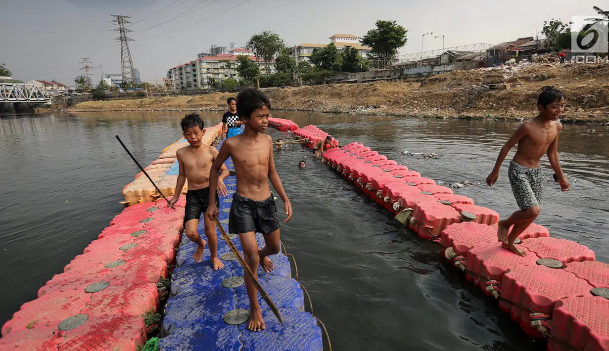Anak-anak membawa bambu runcing untuk mencari ikan di Kanal Banjir Barat (KBB) Petamburan, Jakarta, Senin (12/8/2019). Anak-anak memanfaatkan waktu pulang sekolah mereka untuk berenang dan mencari ikan di KBB saat musim kemarau. (Liputan6.com/Fery Pradolo)