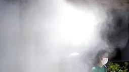 Seorang wanita mengenakan masker untuk mencegah penyebaran Covid-19 di bawah titik kabut dingin di Tokyo (12/8/2020). Menurut Badan Meteorologi Jepang, cuaca panas telah ditetapkan dengan suhu naik lebih dari 34 derajat Celcius (93,2 derajat Fahrenheit) di Tokyo. (AP Photo/Eugene Hoshiko)