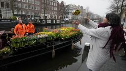 Seorang wanita menangkap buket bunga tulip gratis di Amsterdam, Belanda, Sabtu (15/1/2022). Suasana ibu kota Belanda semakin diringankan oleh garis-garis warna dalam bentuk dari ribuan tandan tulip gratis yang dibagikan para petani yang berlayar dengan perahu melalui kanal. (AP Photo/Peter Dejong)