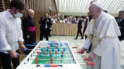 Foto selebaran pada 18 Agustus 2021 menunjukkan Paus Fransiskus bermain foosball atau sepak bola meja dengan Natale Tonini dari asosiasi amatir sepak bola meja Tuscany di sela audiensi mingguan di Vatikan. Paus Fransiskus memang dikenal hobi bermain dan menonton sepak bola. (HO/VATICAN MEDIA/AFP)