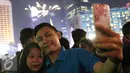 Pengunjung berselfie dengan latar belakang kembang api di kawasan Bundaran HI, Jakarta, Sabtu (31/12). Antusiasme warga menyambut tahun 2017 diramaikan dengan pesta kembang api di sejumlah sudut Ibu Kota. (Liputan6.com/Immanuel Antonius)