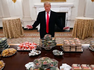 Presiden Amerika Serikat (AS) Donald Trump berpose dengan meja penuh makanan cepat saji di Gedung Putih, Washington, Senin (14 /1). Jamuan Trump ini untuk menyambut juara nasional sepak bola antarkampus, Clemson Tigers. (AP Photo/Susan Walsh)