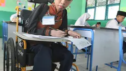 Fauzan Akmal Maulana menunggu pelaksanaan try out ujian di SMP 1 Terbuka Tangerang Selatan, Jumat (22/3). Remaja 15 tahun ini sudah sejak kecil menderita otot lemah, namun masih setiap hari semangat berangkat sekolah. (merdeka.com/Arie Basuki)