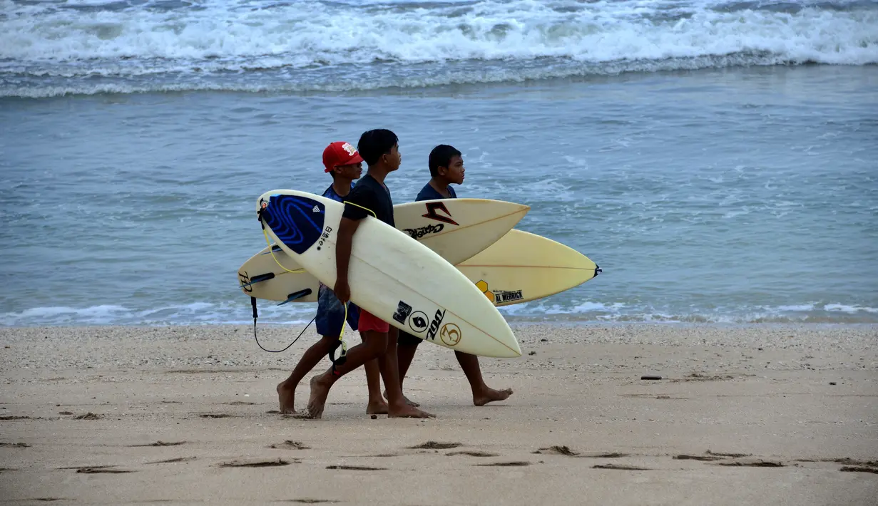 Anak-anak berjalan dengan papan selancar mereka di pantai Kuta di pulau resor Bali (4/10/2021). Pemerintah akan menyiapkan hotel-hotel yang dipersiapkan untuk karantina. (AFP/Sony Tumbelaka)