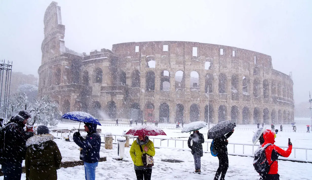 Sejumlah wisatawan mengabadikan Colosseum kuno saat hujan salju di Roma, Italia (26/2). (AFP Photo/Vicenzo Pinto)