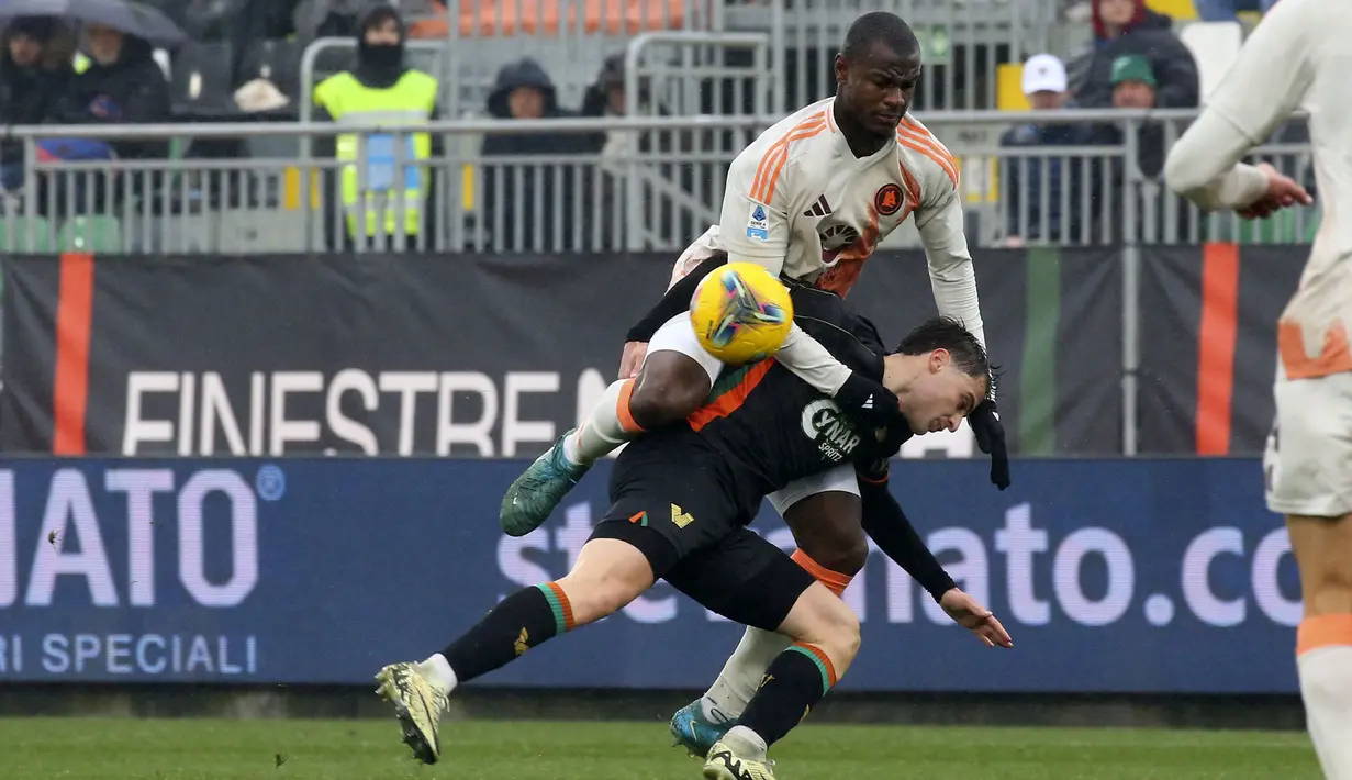 Pemain AS Roma, Evan Ndicka (atas) berebut bola dengan pemain Venezia, Alessio Zerbin dalam laga lanjutan Liga Italia 2024/2025 di Pier Luigi Penzo Stadium, Venice, Italia, Minggu (10/02/2025). (AP Photo/LaPresse/Paola Garbuio)