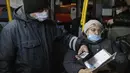 Seorang petugas (kiri) memeriksa kode QR penumpang yang membuktikan tidak adanya infeksi virus corona pada layar ponsel pintar, di dalam bus di Kazan, Senin (22/11/2021). Kazan, menjadi yang pertama di Rusia yang mulai mewajibkan bukti vaksinasi sebelumnya untuk akses transportasi umum. (AP Photo)