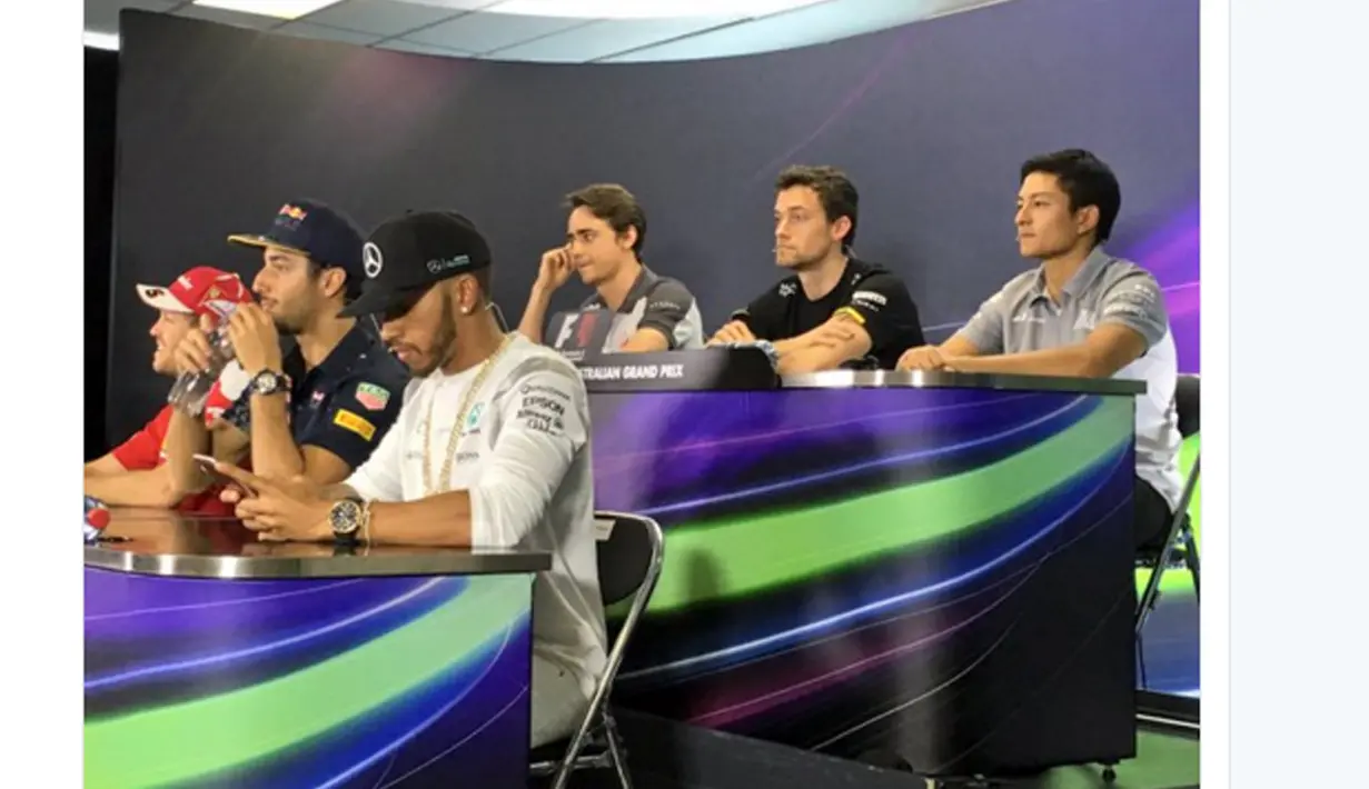 Rio Haryanto terlihat duduk santai diatas Lewis Hamilton dan Sebastian Vettel saat mengikuti sesi press conference jelang balapan Formula 1 2016 di Sirkuit Alber Park, Australia, Kamis (17/3/2016). (bola.com/Twitter/Manor Racing)