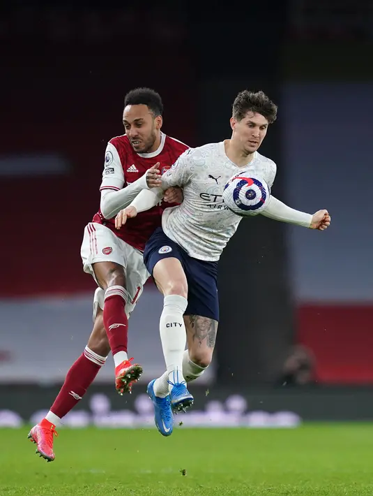 Striker Arsenal, Pierre-Emerick Aubameyang (kiri) bersaing dengan bek Manchester City, John Stones pada lanjutan Liga Inggris di Emirates Stadium, Minggu (21/2/2021). Manchester City kian mengokohkan posisinya di puncak klasemen setelah menang 1-0 di kandang Arsenal. (John Walton / POOL / AFP)