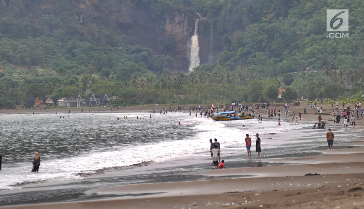 Wisawatan memadati  Pantai Palangpang dengan latar belakang curug di Kecamatan Ciemas, Kabupaten Sukabumi, Selasa (26/6). Pantai Palangpang atau yang biasa disebut Teluk Ciletuh berada di titik utama Geopark Ciletuh-Palabuhanratu (Merdeka.com/Arie Basuki)