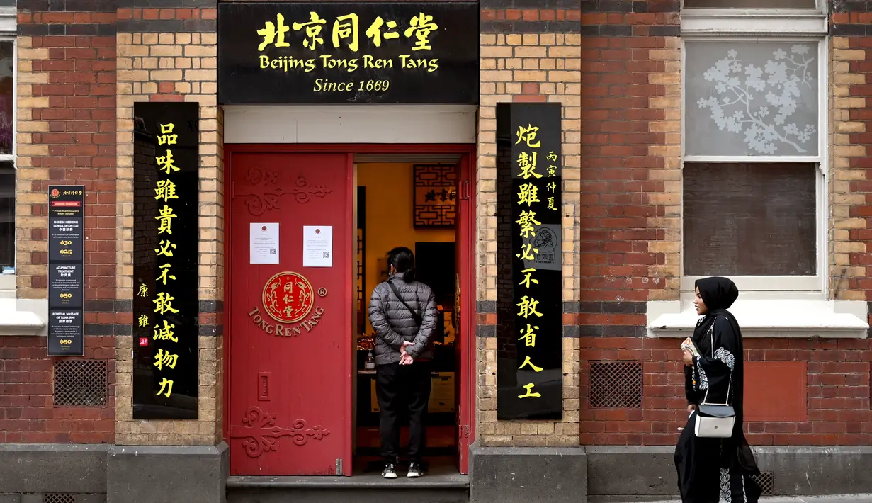 Seorang perempuan berjalan melewati sebuah restoran di jalan yang sepi ketika yang lain menunggu pesanan takeaway di Chinatown Melbourne ketika kota itu bersiap untuk mencabut beberapa pembatasan pada akhir pekan ini setelah mengalami lockdown keenam, Selasa (19/10/2021). (William WEST/AFP)
