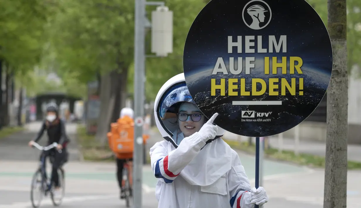 Seorang pesepeda diperlihatkan peringatan untuk mengenakan helm oleh siswa berkostum astronaut, di Ring Street, Wina, Austria, Rabu (5/5/2021). Delapan siswa Wina berpartisipasi dalam acara tersebut untuk mengingatkan pengendara sepeda mengenakannya helm demi keamanan mereka. (JOE KLAMAR/AFP)