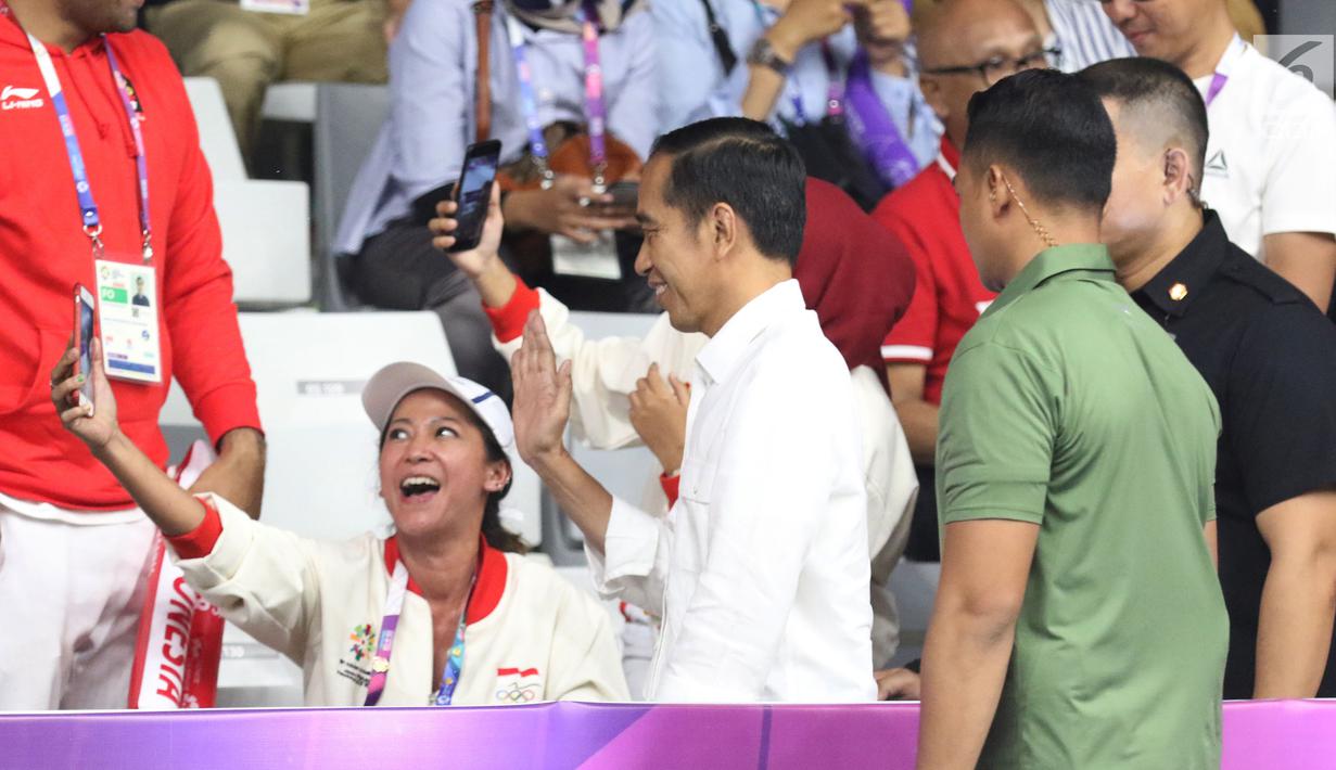 Presiden Jokowi menyapa penonton saat tiba untuk menyaksikan Final Bulutangkis Beregu Putra Asian Games 2018 antara Indonesia melawan China di Jakarta, Rabu (22/8). (Liputan6.com/Helmi Fithriansyah)