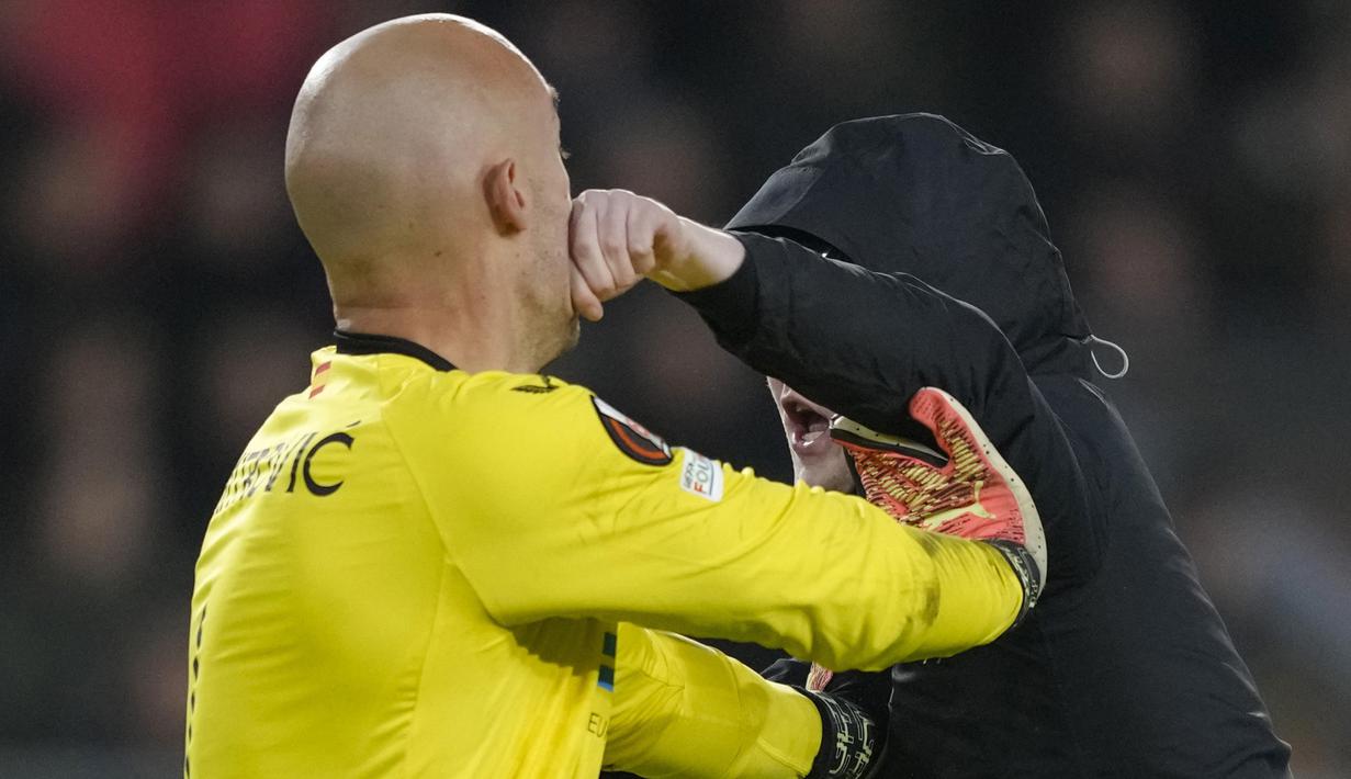 <p>Seorang suporter fanatik PSV melepaskan pukulan ke arah kiper Sevilla, Marko Dmitrovic dalam laga leg kedua babak playoff fase gugur Liga Europa 2022/2023 di Philips Stadium, Eindhoven, Jumat (24/2/2023). (AP Photo/Peter Dejong)</p>
