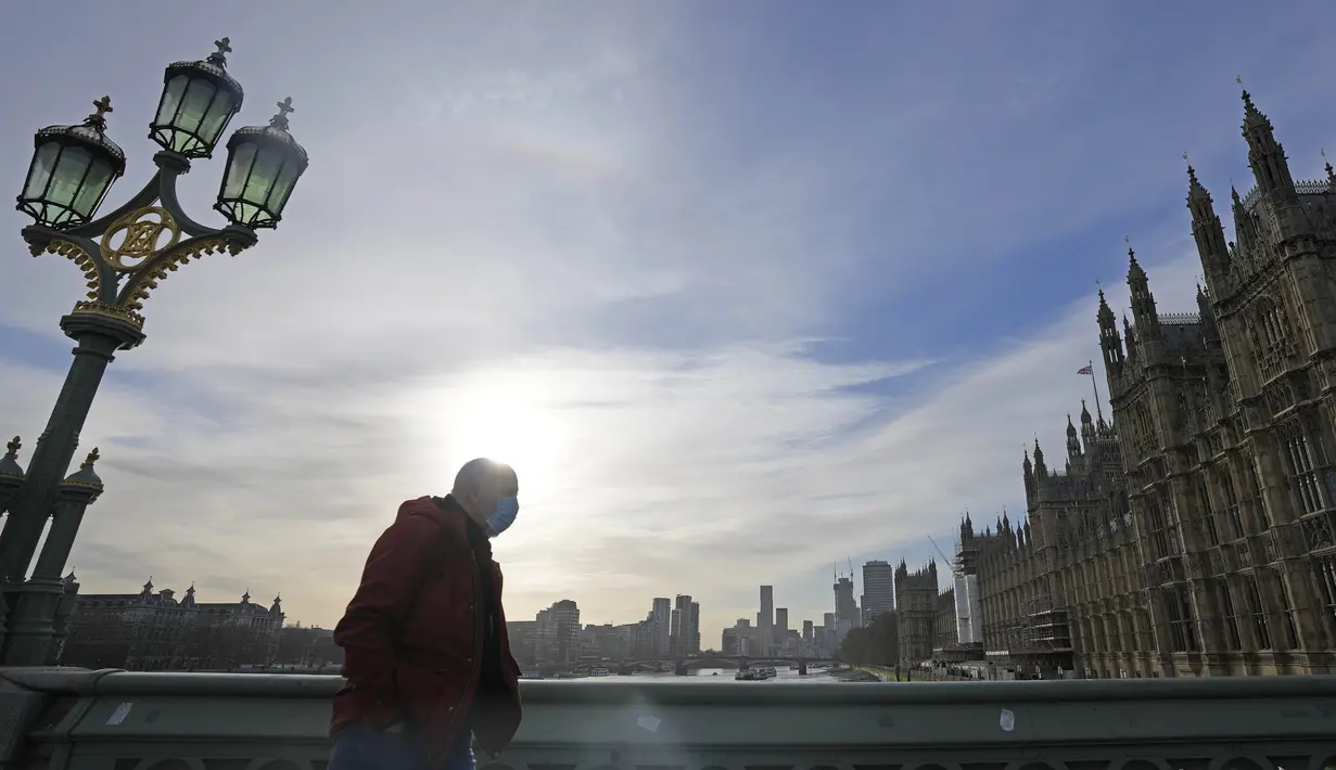 Seorang pria bermasker melintasi Jembatan Westminster di London, Kamis (9/12/2021). Perdana Menteri Inggris Boris Johnson kembali mendesak orang untuk bekerja dari rumah dan kewajiban menunjukkan sertifikat vaksin untuk memasuki klub malam dan tempat dengan kerumunan besar. (AP Photo/Frank Augstein)