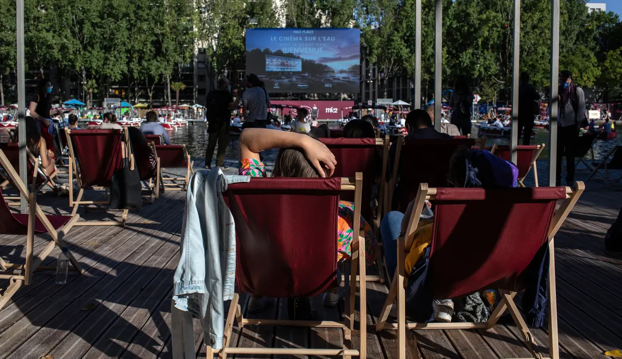 Orang-orang menghadiri Cinema on the Water, yang diselenggarakan Paris Plages selama pemutaran "Le Grand Bain" di Paris, Prancis pada 18 Juli 2020. Paris menghadirkan terobosan baru dengan bioskop terapung lengkap dengan perahu yang tetap menjaga jarak. (AP Photo/Rafael Yaghobzadeh)
