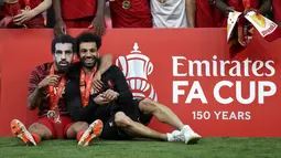 Gelandang Liverpool Thiago mengenakan topeng Mohamed Salah dan meemluk rekannya tersebut setelah mereka memenangkan partai final Piala FA atas Chelsea di Stadion Wembley pada Minggu (16/5/2022) dini hari WIB. Liverpool sukses menjuarai Piala FA 2021/2022 mengalahkan Chelsea lewat adu penalti 6-5. (AP Photo/Ian Walton)