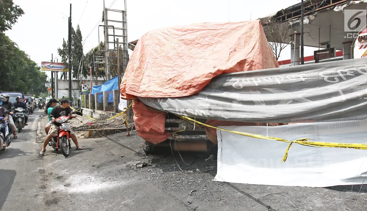 Garis polisi terpasang dekat bangkai truk tangki yang terbakar di SPBU Jalan Kahfi 2, Jagakarsa, Jakarta, Sabtu (30/12). Saat terbakar, truk yang kini ditutup terpal oranye itu diketahui memuat bahan bakar jenis pertalite. (Liputan6.com/Herman Zakharia)