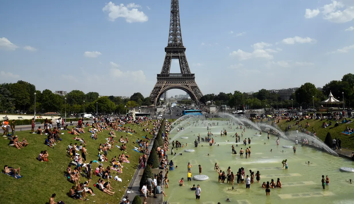 Turis dan warga menyejukkan diri dan berjemur di kolam Trocadero Fountains (air mancur Trocadero) dekat Menara Eiffel di Paris, Kamis (25/7/2019). Gelombang panas di Eropa mencapai puncaknya, bahkan suhu di ibu kota Prancis mencapai di atas 41 derajat Celcius. (Bertrand GUAY / AFP)