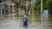 Seorang pria mengarungi jalan yang banjir di Hulu Langat, di luar Kuala Lumpur, Malaysia, Minggu (19/12/2021). Kuala Lumpur dan perkampungan sekitarnya dilanda banjir akibat hujan deras selama dua hari, menyebabkan ribuan warga mengungsi dan banyak jalan yang memutus akses. (AP Photo/Vincent Thian)