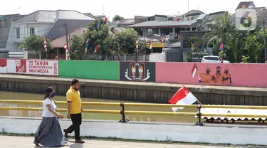 Warga berjalan di depan mural bertema Kemerdekaan RI pada dinding turap Sungai Ciliwung di kawasan Kampung Melayu, Jakarta, Minggu (16/8/2020). Mural karya petugas Pekerja Penanganan Sarana dan Prasarana Umum (PPSU) itu dibuat dalam rangka memeriahkan HUT ke-75 RI. (Liputan6.com/Immanuel Antonius)