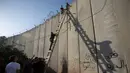 Suasana saat pemuda Palestina menggunakan tangga saat memanjat tembok pembatas Israel dalam perjalanan menuju Masjid Al Aqsa untuk mengikuti salat Jumat terakhir di bulan Ramadhan, Al-Ram, Utara Yerusalem, Jumat (8/6). (AP Photo/Majdi Mohammed)