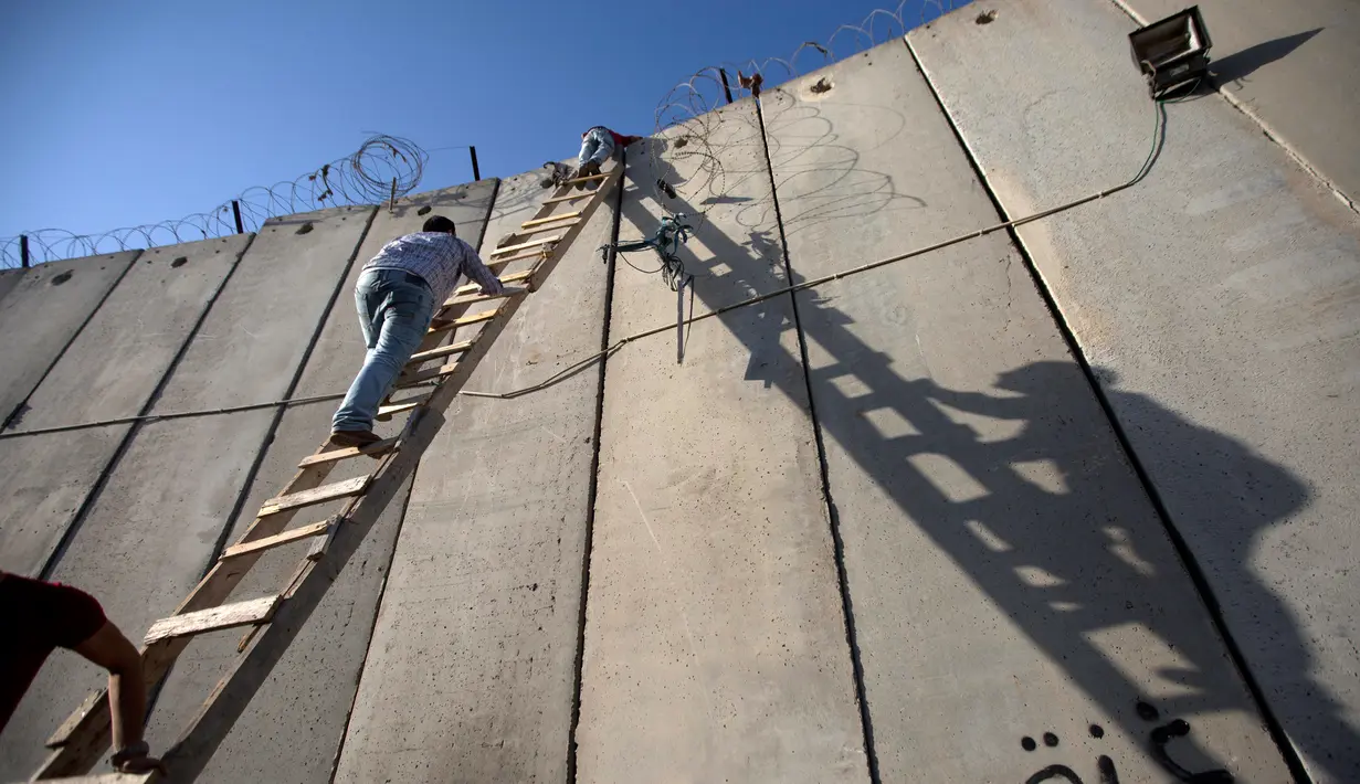 Pemuda Palestina menggunakan tangga saat memanjat tembok pembatas Israel dalam perjalanan menuju Masjid Al Aqsa untuk mengikuti salat Jumat terakhir di bulan Ramadhan, Al-Ram, Utara Yerusalem, Jumat (8/6). (AP Photo/Majdi Mohammed)