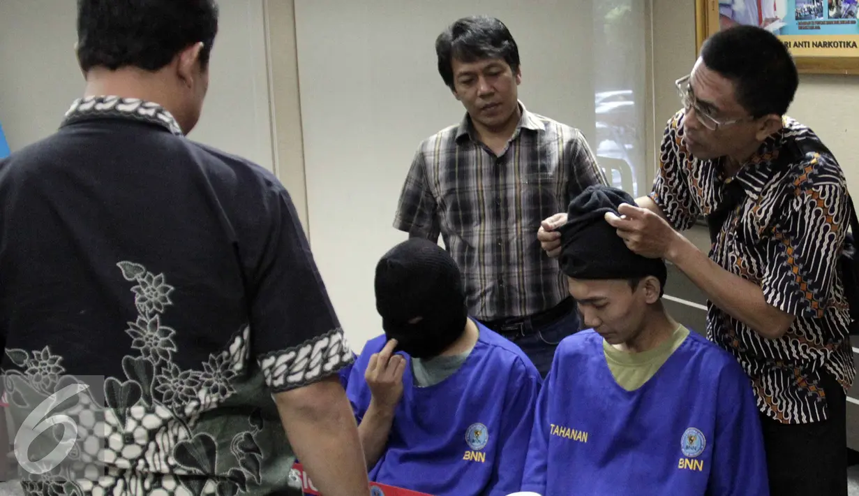 Petugas memakaikan penutup muka ke tersangka  saat rilis penangkapan 6.642 gram narkotika golongan 1 jenis sabu di gedung BNN, Jakarta, Jumat (7/8/2015). Empat tersangka merupakan jaringan Internasional asal Nigeria. (Liputan6.com/Helmi Afandi)