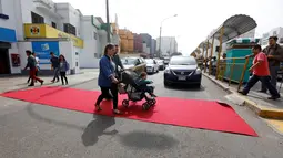 Warm berjalan di atas karpet merah yang terbentang di salah satu ruas jalan di distrik Magdalena del Mar, Lima, Peru, (2/7). Aksi ini dilakukan untuk menggugah kesadaran warga perkotaan agar menghormati pejalan kaki. (REUTERS / Guadalupe Pardo)