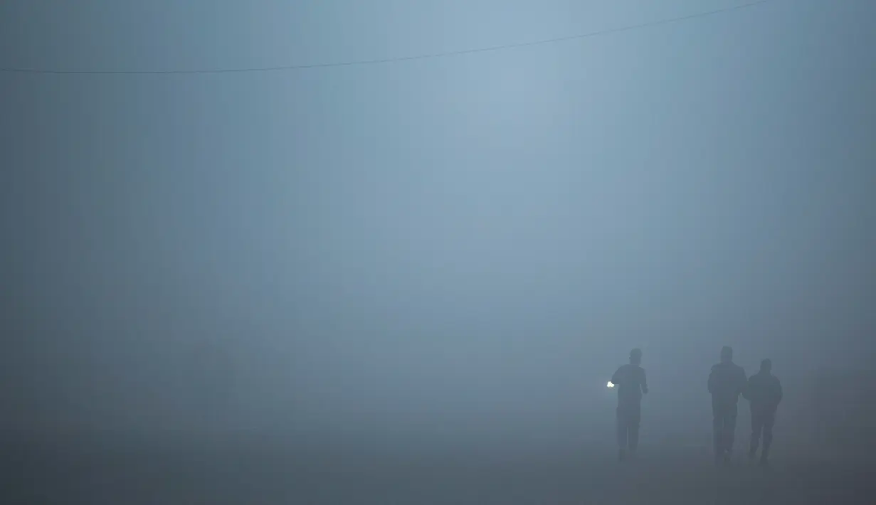 Seorang pria berlari di sepanjang jalan dalam kondisi berkabut akibat suhu dingin di New Delhi, Senin (30/12/2019). New Delhi, ibu kota India, saat ini mengalami musim dingin dengan hari dingin terpanjang dalam 22 tahun terakhir. (Photo by Jewel SAMAD / AFP)