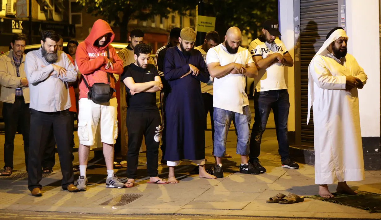 Sejumlah pria muslim melaksanakan salat di lokasi sebuah van yang menabrak pejalan kaki di Finsbury Park Road, London utara, Senin (19/6). Polisi menyebut van menabrak kerumunan orang yang baru selesai salat di masjid Finsbury Park (Yui Mok/PA via AP)