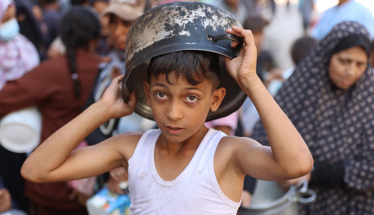 Seorang anak laki-laki Palestina mengantri untuk menerima jatah makanan, yang ditawarkan oleh sebuah badan amal, di kamp pengungsi Al-Shati di Gaza pada 17 Oktober 2024. (Omar AL-QATTAA/AFP)
