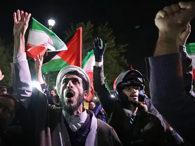 Para pengunjuk rasa mengibarkan bendera Iran dan bendera Palestina saat mereka berkumpul di depan Kedutaan Besar Inggris di Teheran pada tanggal 14 April 2024. (ATTA KENARE/AFP)