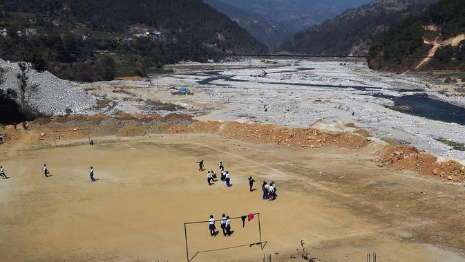 Anak-anak sekolah bermain sepak bola di lapangan yang berada di Bahuneypati, Sindhupalchok, sekitar 70 Kilometer timur laut Kathmandu, Nepal, 15 Februari 2018. Di sini kita bisa bermain bola di antara pegunungan Nepal yang megah. (PRAKASH MATHEMA/AFP)