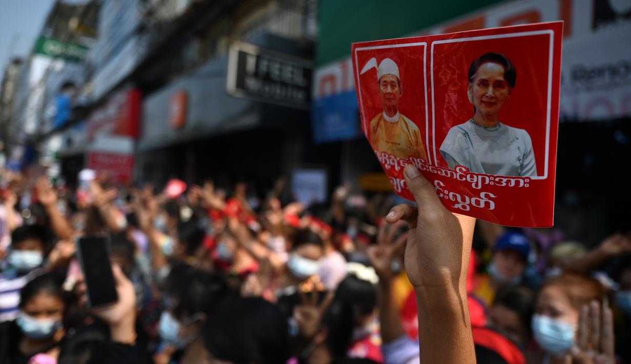 Seorang pengunjuk rasa memegang poster dengan gambar pemimpin terpilih Aung San Suu Kyi (kanan) yang ditahan dan presiden Win Myint saat demonstrasi menentang kudeta militer di Yangon, Myanmar pada Sabtu (6/2/2021).  Ribuan orang turun ke jalan-jalan untuk melawan kudeta. (YE AUNG THU / AFP)