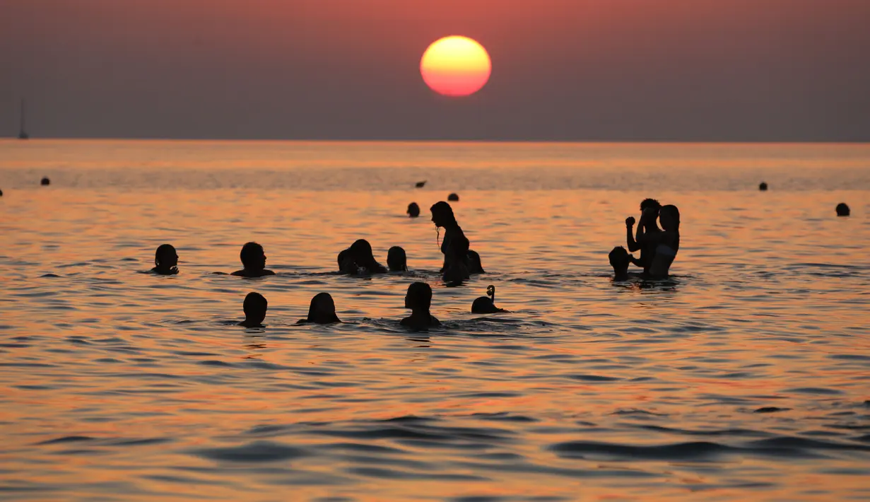 Pengunjung berenang sambil menikmati pemandangan matahari terbenam di Pantai Santa Maria Del Focalo, Pulau Sisilia, Italia, 7 Agustus 2017. Pantai Santa Maria Del Focalo menjadi salah satu tujuan objek wisata favorit di Italia. (ludovic MARIN/AFP)