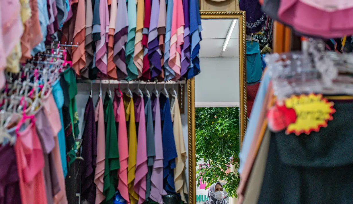 Pekerja mengenakan masker sebagai tindakan pencegahan Covid-19 terlihat di cermin di dalam tokonya yang menjual pakaian budaya Malaysia yang disebut Baju Melayu dan Baju Kurung menjelang Idul Fitri yang menandai berakhirnya bulan suci Ramadan di Kuala Lumpur (13/5/2020). (AFP/Mohd Rasfan)