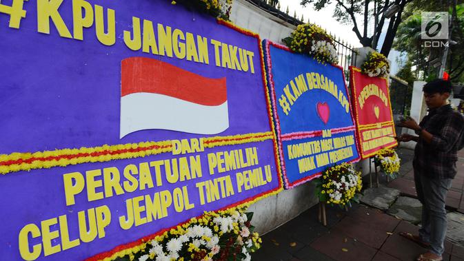 Warga berdiri dekat karangan bunga yang ada di Gedung Komisi Pemilihan Umum (KPU), Jakarta, Sabtu (20/4). Karangan bunga terus berdatangan ke Gedung KPU. (merdeka.com/Imam Buhori)