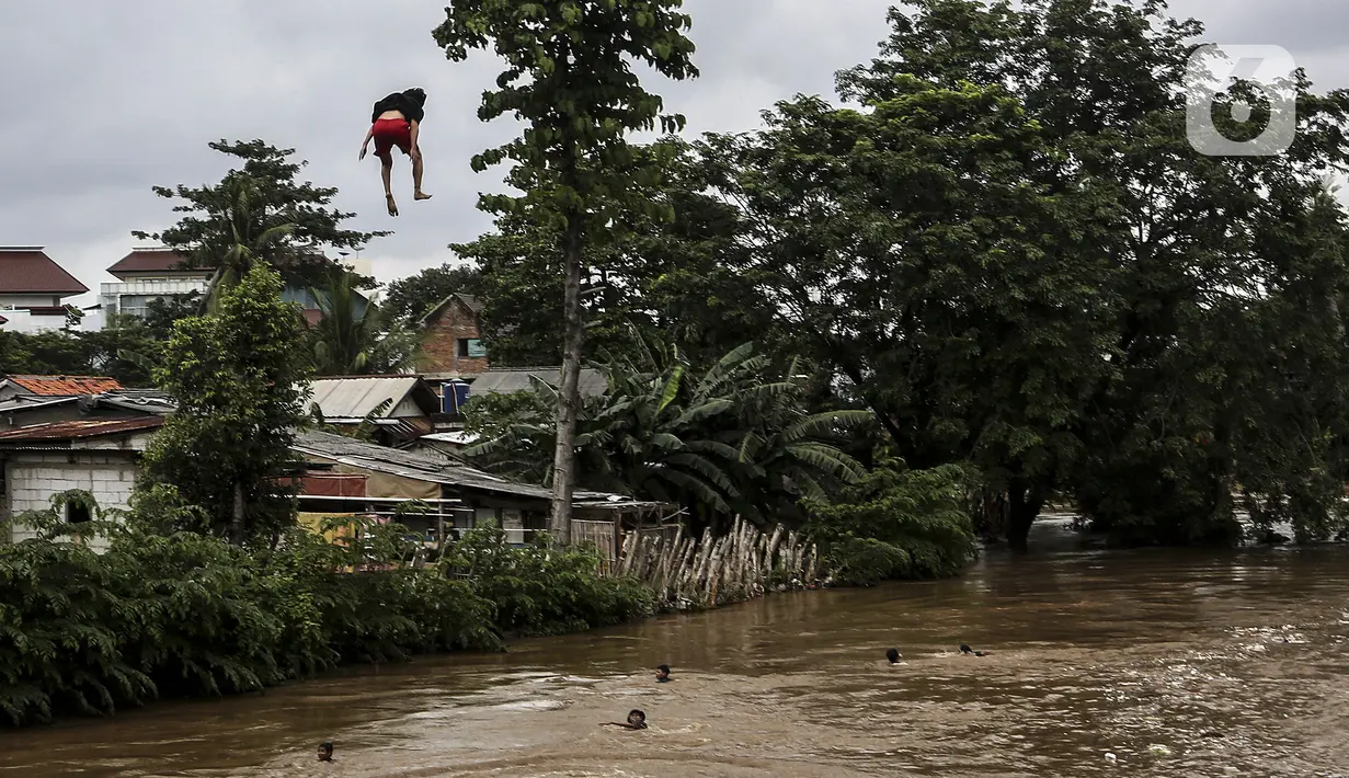 Anak-anak melompat ke Sungai Ciliwung saat banjir melanda Jalan Bina Warga Rt 005/Rw 07 Kelurahan Rawa Jati, Jakarta, Senin (8/2/2021). Banjir setinggi 60-190 cm tersebut disebabkan oleh luapan air Sungai Ciliwung dan curah hujan Jakarta yang tinggi. (Liputan6.com/Johan Tallo)